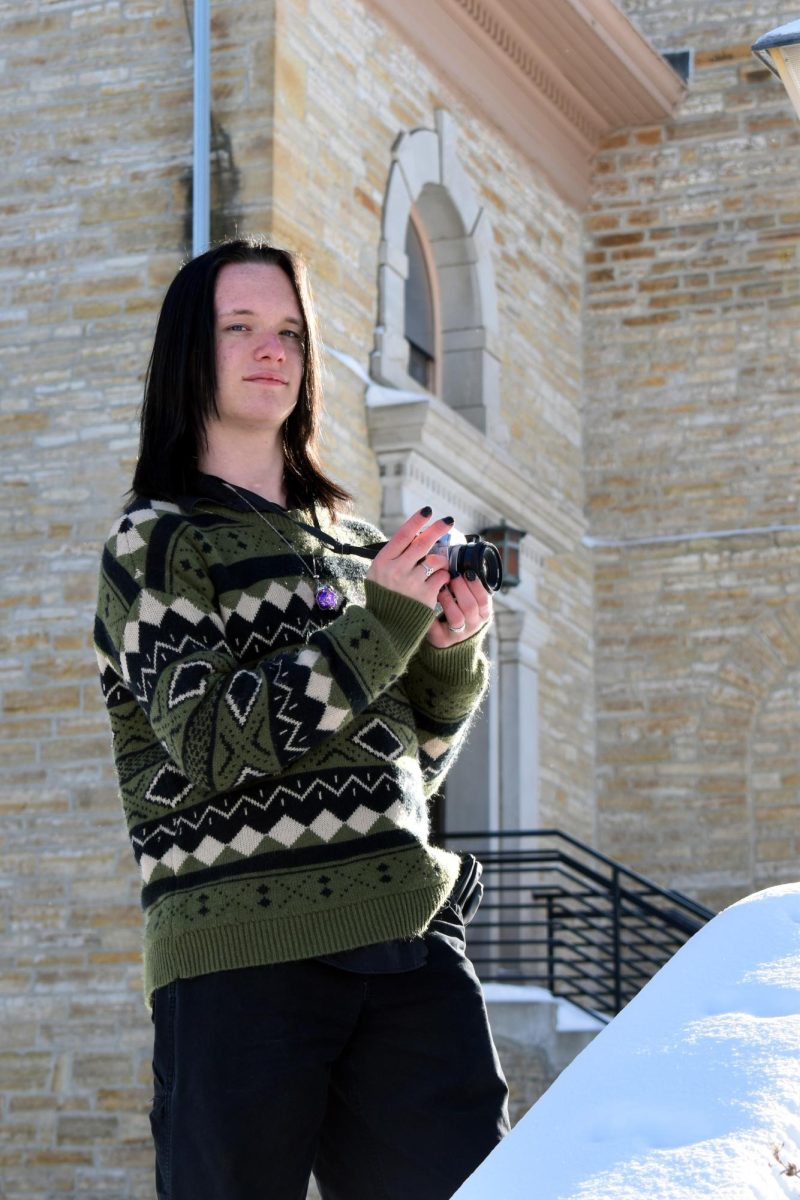 Aspen poses with a film camera in front of a church-style structure